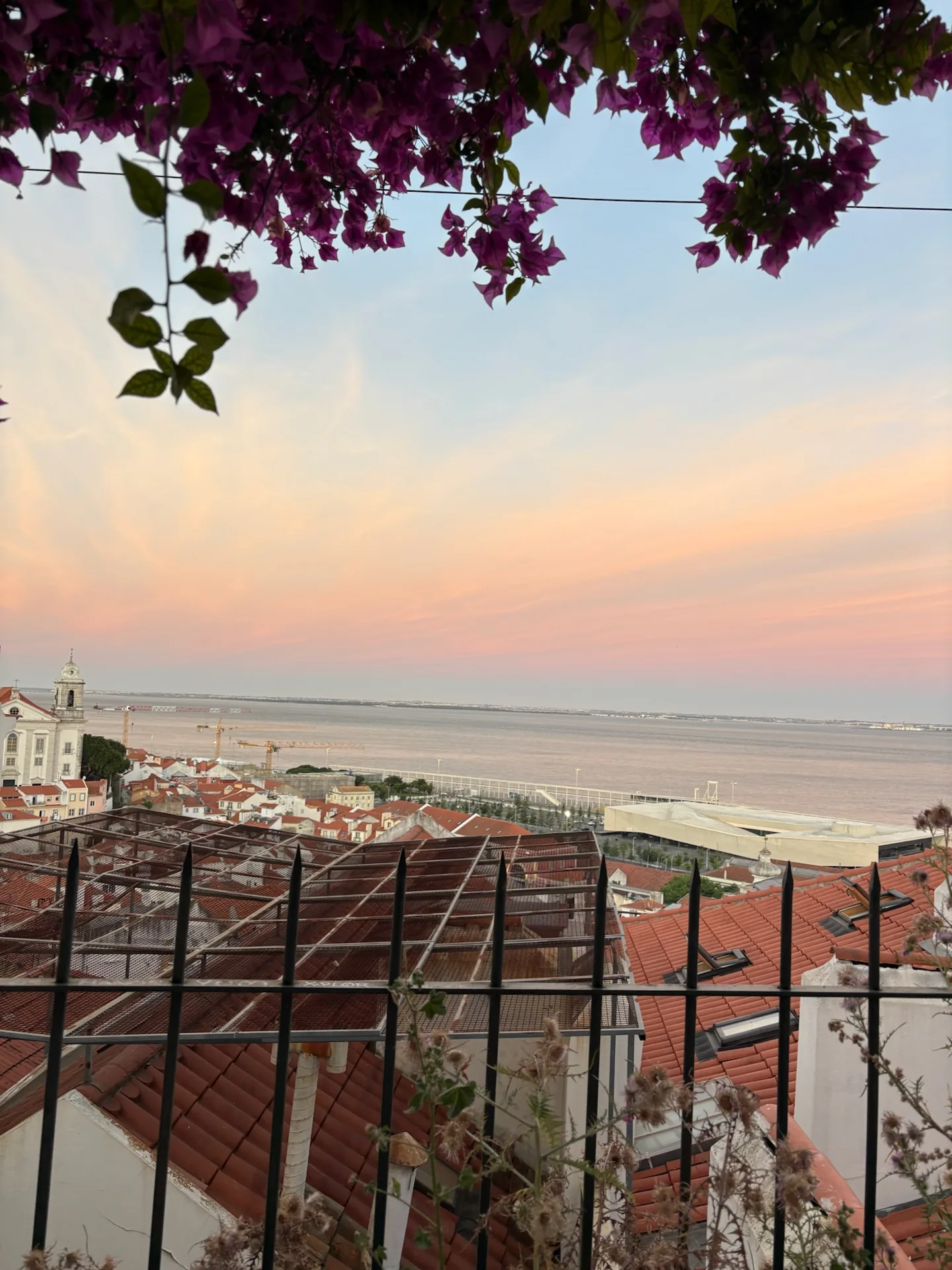 Lisbon rooftops and the river beneath a pink evening sky