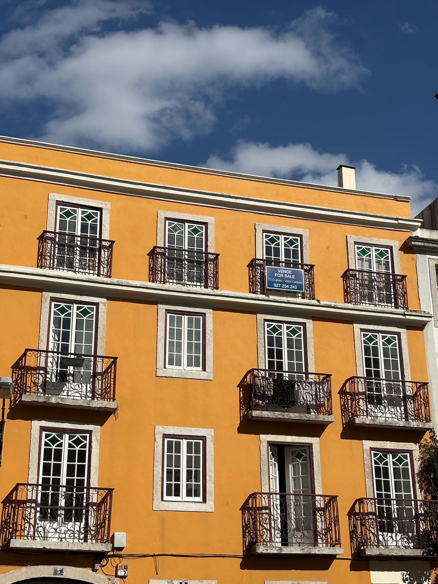 A sunlit yellow building with wrought-iron balconies in Lisbon